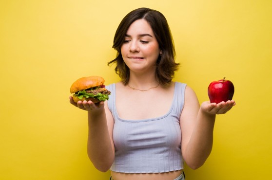 Una noia dubtant si menjar una hamburguesa o una poma.